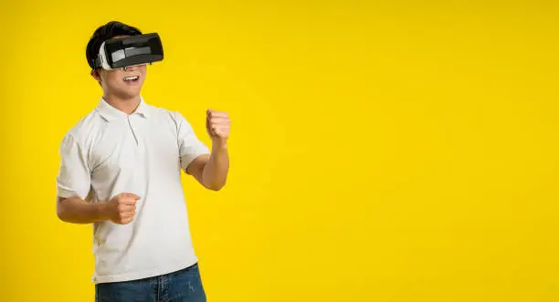 Portrait of young asianman play ing virtual reality on yellow  background