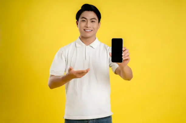 Portrait of young asianman using phone on yellow background