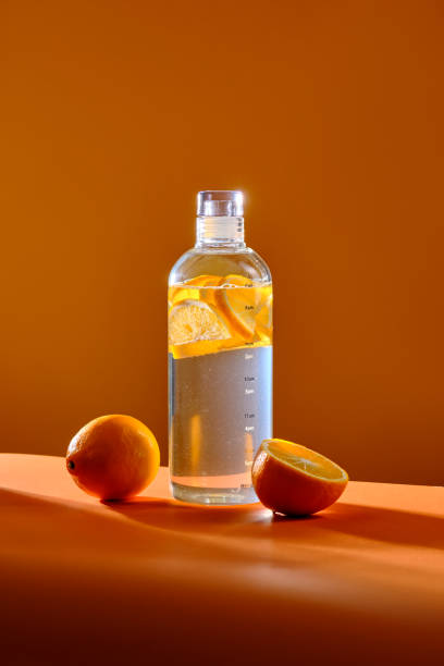 butelka szklana z cytryną na pomarańczowym tle. - water bottle purified water water drink zdjęcia i obrazy z banku zdjęć