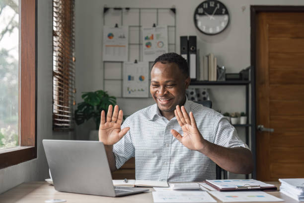 istock Video call. Cheerful attractive African American guy is using laptop for video communication, waving into webcam and talking online 1475716475