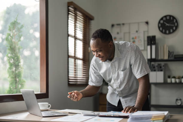 istock Happy African man using laptop computer and calculator for calculating invoice at home 1475716570