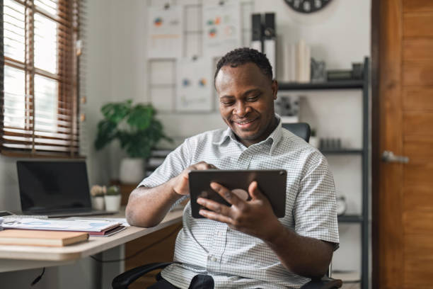 웃고 있는 아프리카계 미국인 프리랜서는 집에서 새 프로젝트에서 작업하는 동안 스크린 디지털 태블릿을 만지고 있습니다. 인터넷에서 정보를 찾는 흑인 사업가 - telephone network control room 뉴스 사진 이미지