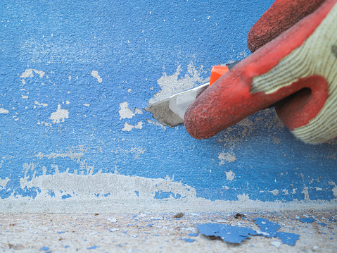 Close up, clean and prepare the old wall surface. by hand holding the cutter blade Make a blue scrape on the old wall to repair the old wall that has deteriorated before painting a new one.