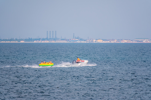 Tubers on their donuts being towed behind a power boat on a dam for recreational fun. Etreme power motor boat cruising donut in high speed. Mediterranean colors in tropical turquoise bay.