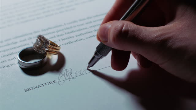 Caucasian Hand Signs Signature on Contract/Application with Wedding Rings