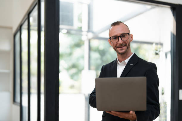 istock businessman handsome smiling using laptop while standing in office 1475721553