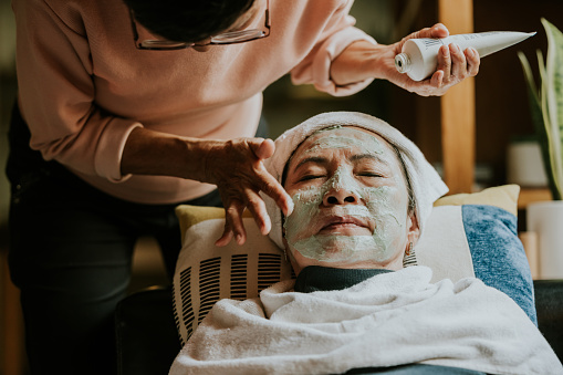 Asian senior adult woman taking care her face and wrinkle with facial mud, applying mud on face.
