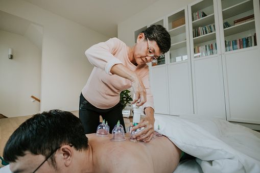 Active senior adult who was a vacuum cupping therapist is treating her patient from back pain.