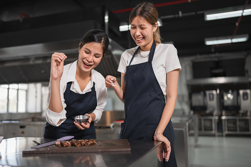 Two happy Asia woman assistant chef cooking with steak at kitchen background