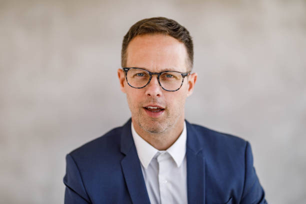 Portrait of fashionable man in eyeglasses, blue suit and golden chain on grey