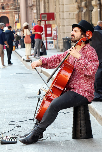 Bologna - Italy - April 16, 2022: Street performer, playing cello in the historic downtown district of Bologna. Busking on street concept.
