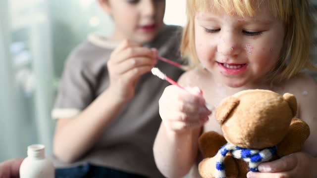 Little boy applies antiseptic medicine to his ill sister with chickenpox while she is playing doctor with his toy bear