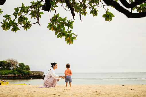 asian woman with her baby sitting on the sand and enjoy the sunset