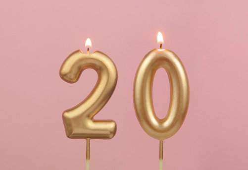 Burning golden birthday candles on pink background, number 20
