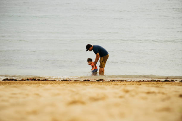 istock asian man teaching his baby walking on the beach 1475759186