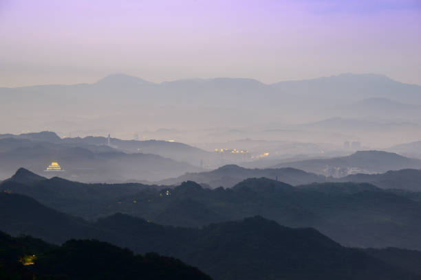 Stunning dusk scenery - vibrant white sky, dynamic clouds, misty mountains. Serene Ocean Surrounding the Coastal Village of Jiufen in Taiwan.