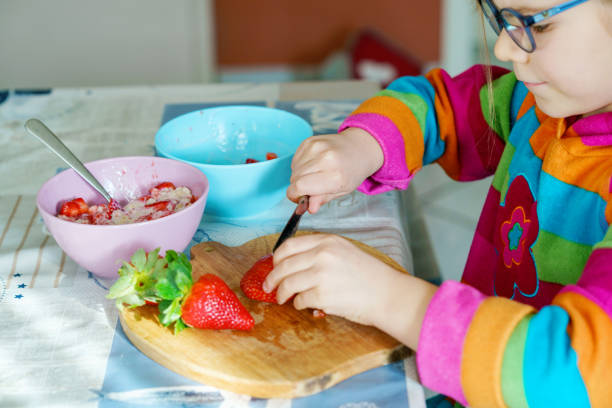istock Littl preschool learning how to use a knife cutting strawberry making fruit salad for porridge for breakfast in the kitchen. Healthy food for children. 1475764457
