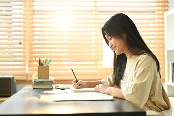 istock Smiling asian teen girl making notes, ding essay homework assignment at home. Learning and education concept. 1475765042