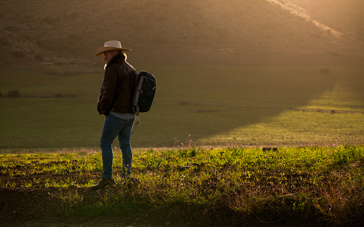 Adult man in cowboy hat standing on hill against mountain during sunrise