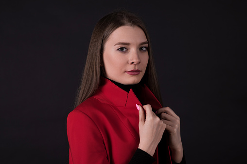 Portrait of a young and attractive Caucasian businesswoman in a red suit isolated on a black studio background.