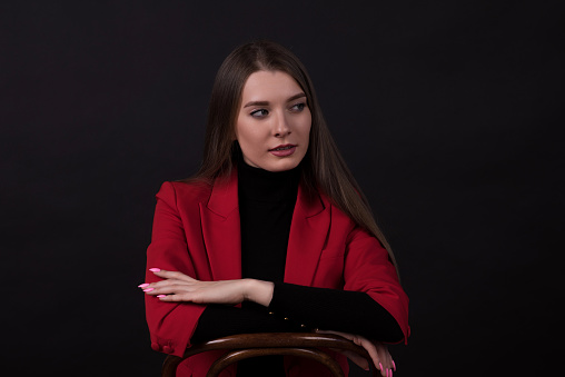 Portrait of a young and attractive Caucasian businesswoman in a red suit isolated on a black studio background.