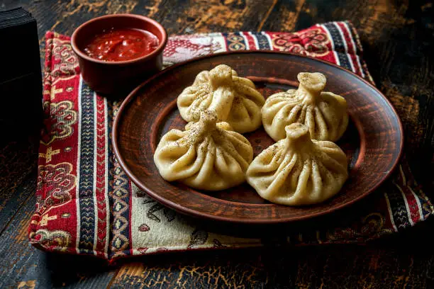 Photo of Khinkali with meat filling in a plate. Georgian dumplings in a composition with sauce and vegetables