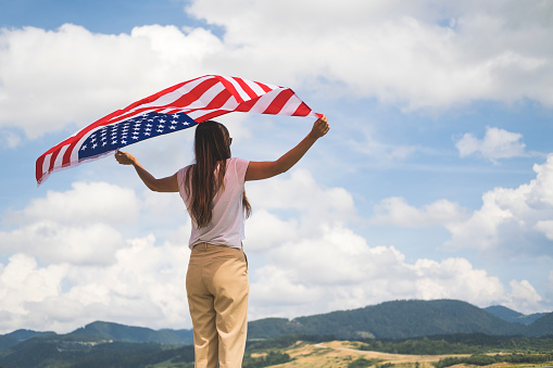 Rear view of a woman waving an American flag at the lake, summertime.