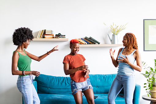 Three Black female friends listening to music and dancing at home
