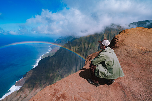 Man looking at rainbow over Na Pali coast in Kauai Hawaii island USA