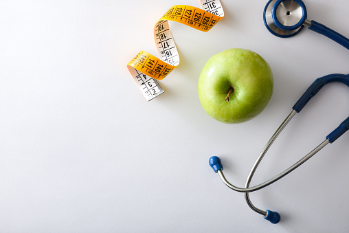 Apple, stethoscope and tape measure on white table representing health, nutrition and body control. Top view.