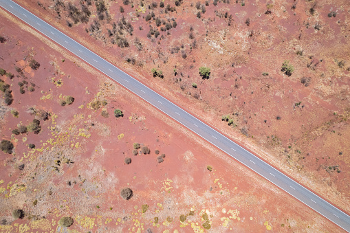 Looking down at the diagonal asphalt road with the red Australian dirt and bushes on both sides of the road