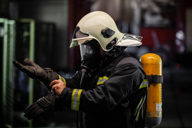 firefighter portrait wearing full equipment with oxygen mask. Putting on protective gloves . fire trucks in the background. stock photo