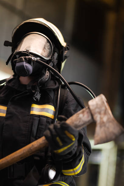 Female firefighter portrait wearing full equipment with oxygen mask and an axe. stock photo