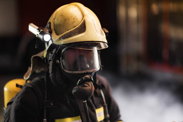 istock Fireman wearing full equipment.  Firefighter with protective helmet oxygen mask and flashlight. Smoke and fire trucks in the background. 1475782094