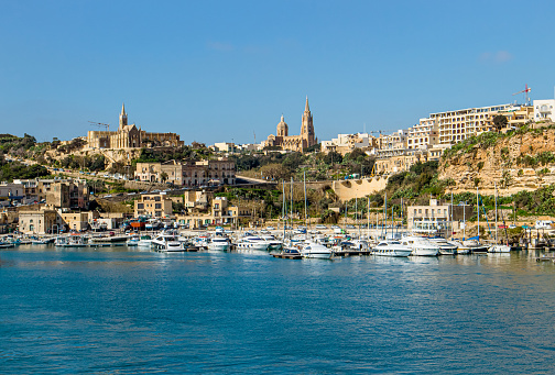 The port of Mġarr on the island of Gozo, Malta. Beautiful city on the cliffs and hills on the background on sunny spring day.