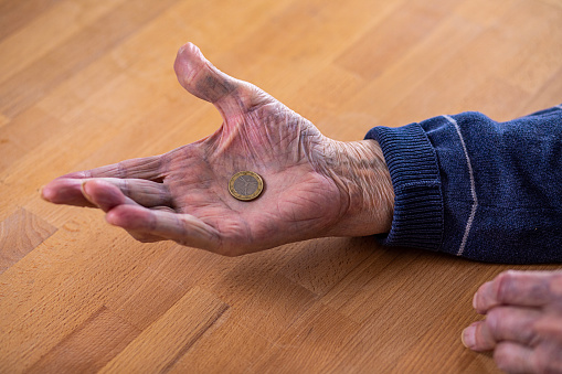 An elderly man holds a coin on his palm . Poverty in times of economic crisis.