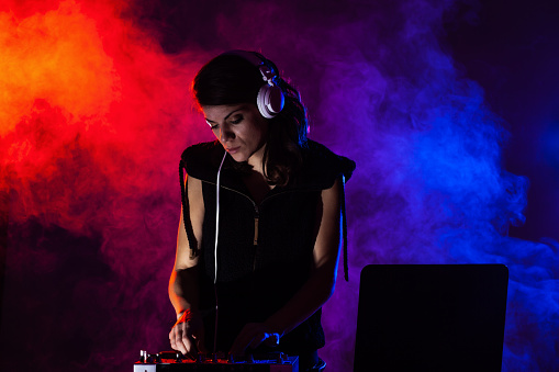 Female DJ playing music on a mixer. Red and blue lights and smoke in the background