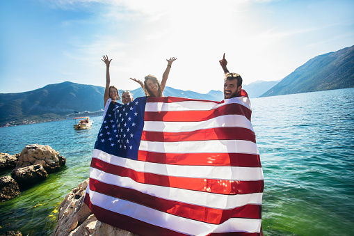 Group of happy friends with american flag on beach-independence day, summer holidays and people concept