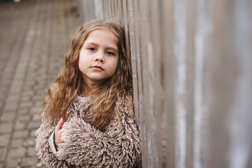 Portrait of a child on a city street. Little girl in an urban setting with sad eyes looks at the camera