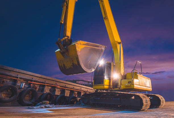 gelber bagger arbeitet daran, rohreis vor dem hintergrund des nachthimmels in den lastkahn im hafen zu transportieren - industrial ship earth mover barge yellow stock-fotos und bilder