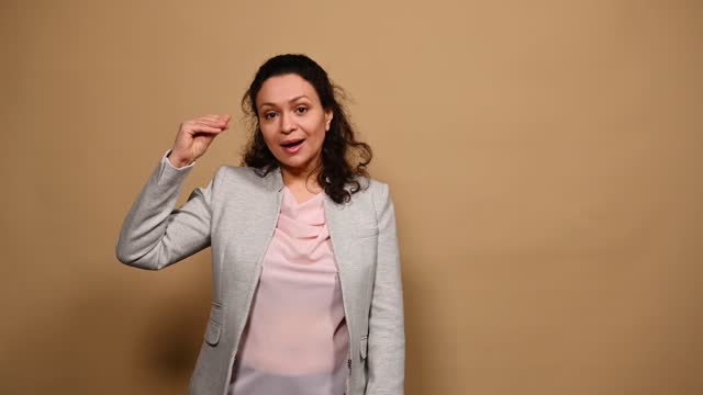 Irritated bored middle-aged woman showing bla-bla-bla gesture with hands, isolated beige background