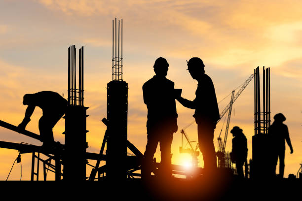 istock Silhouette of Engineer and worker checking project at building site background, construction site at sunset in evening time 1475798473