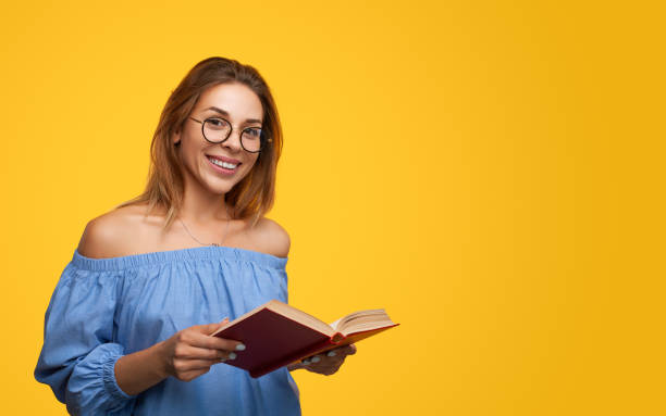 istock Clever young female smiling while reading novel against yellow background 1475800717