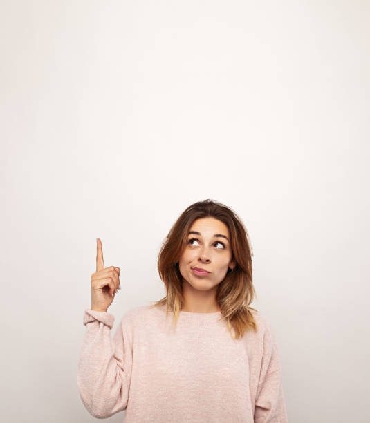 istock Unsure young woman pointing up against white background 1475800745