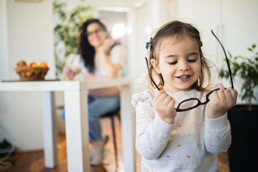 Portrait of a cute little girl playing with her mother's eyeglasses