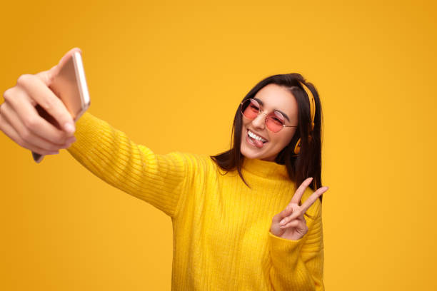 istock Joyful young ethnic lady smiling and showing peace sign while taking selfie 1475804349