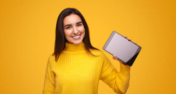 istock Content Hispanic lady showing tablet and smiling in yellow studio 1475804392