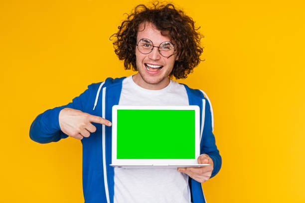 istock Positive guy pointing at netbook with chromakey screen in yellow studio 1475807981
