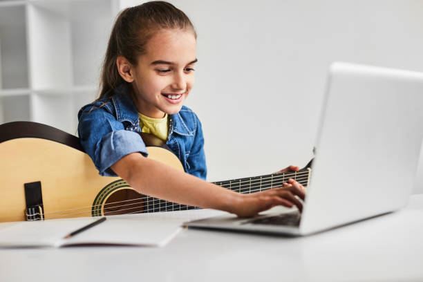 istock Happy child with guitar using laptop during online lesson 1475808116