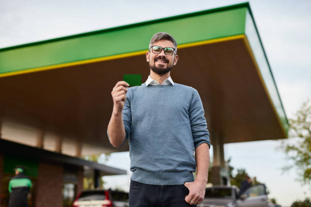 Content bearded man demonstrating plastic card at gas station